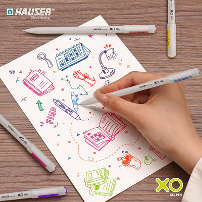 Hand holding a Hauser XO gel pen coloring a sheet with illustrations on a wooden surface.