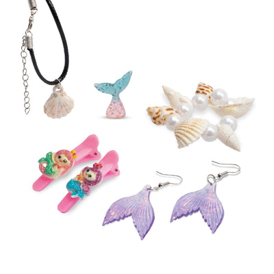 A collection of completed mermaid-themed accessories including a black cord shell necklace, a clear blue mermaid tail charm, a shell and pearl beaded bracelet, two pink mermaid hair clips, and a pair of iridescent purple mermaid tail earrings.