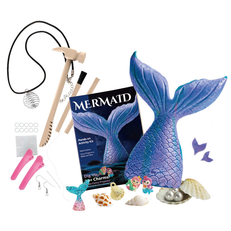 A flat-lay view of all components in the Mermaid Activity Kit, including the instruction booklet, the large mermaid tail dig block, wooden hammer and chisel, brush, necklace cords, earring hooks, hair clips, and various loose shells and pearls.
