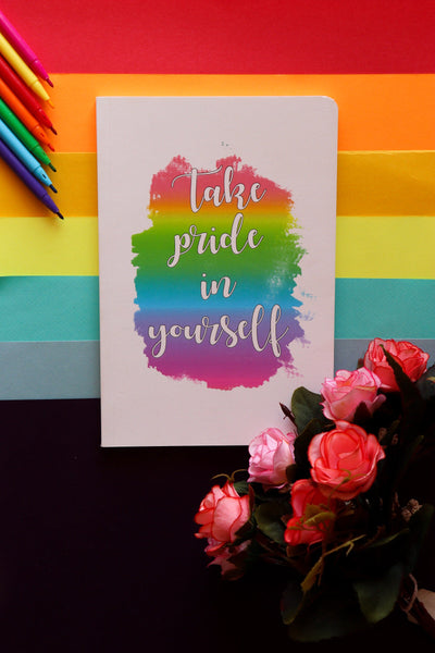 Notebook with 'Take pride in yourself' quote on a colorful striped background with flowers and pencils.