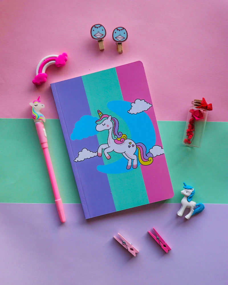 A colorful notebook with a unicorn design on the cover, accompanied by a pen and various small decorative items.